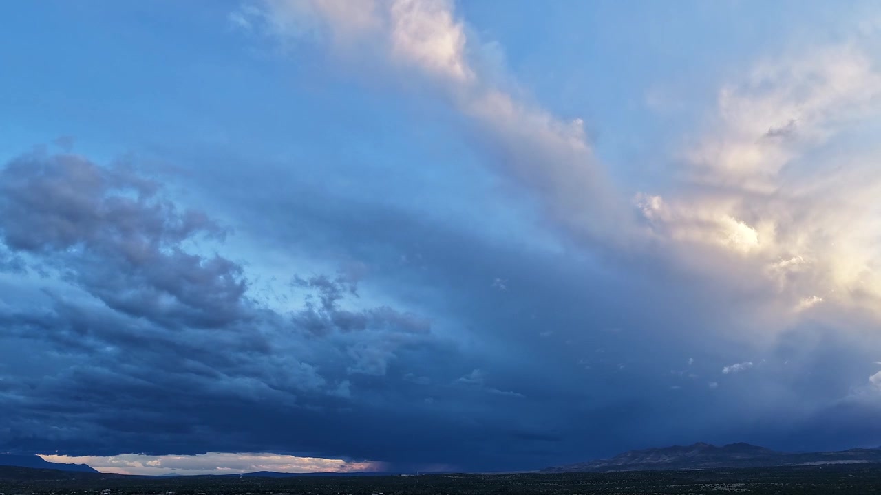 4K drone timelapse captures a fast moving blanket of blue and white clouds over a rugged mountainside at sunset. Cinematic atmospheric motion reveals shifting layers and soft twilight colors.