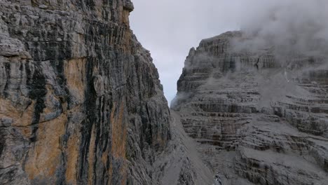 vuelo aéreo a lo largo de montañas rocosas con pendiente empinada cubierta de densas nubes en los alpes