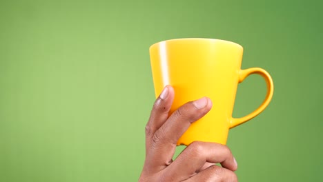 hand holding yellow coffee mug again green background