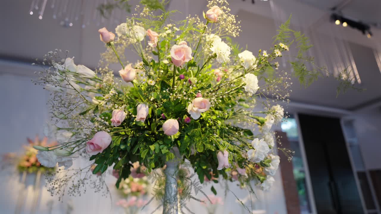 Upward cinematic camera orbit around a floral centerpiece with roses at a well-lit wedding venue