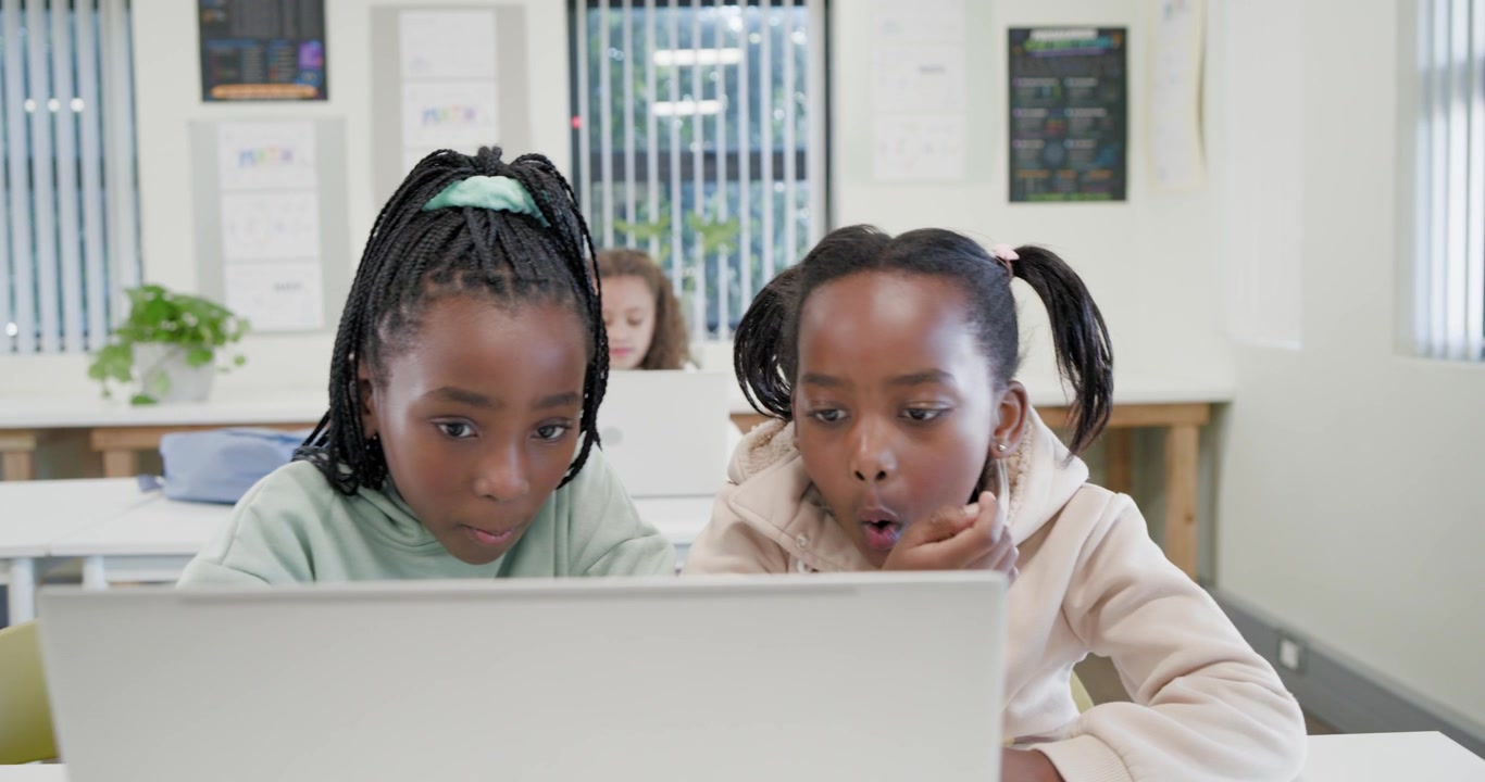 Due studentesse afroamericane chinate sul laptop, che trovano una soluzione e festeggiano il successo