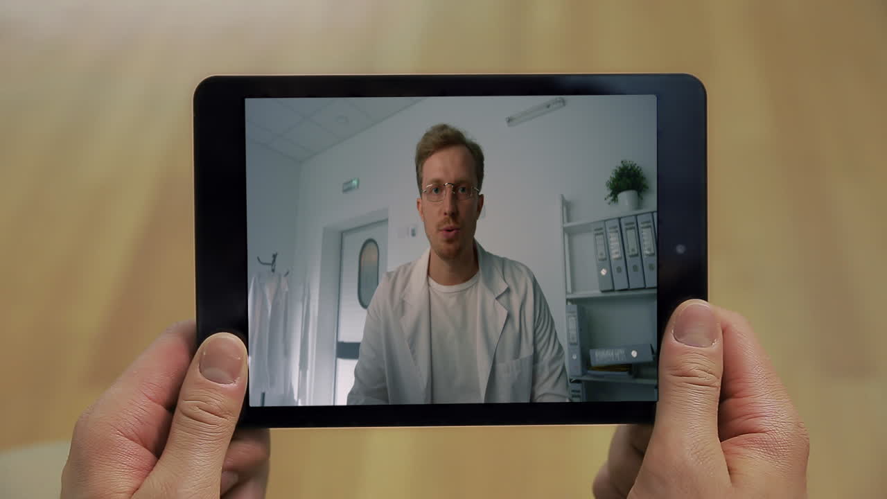 Primo piano di un medico che parla allo schermo di un tablet all'interno di un ospedale. Uomo che effettua una videochiamata