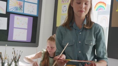 Video-of-concentrating-caucasian-schoolgirl-standing-at-easel-painting-in-art-class,-copy-space