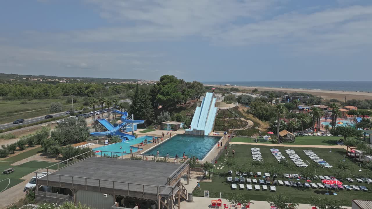 Tourists are enjoying summer vacation at a water park in narbonne, france. The aerial view shows people swimming and sliding in an acrobatic way