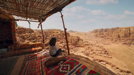 Cinemagraph-Bucle-De-Vídeo-Sin-Interrupciones-De-Una-Mujer-Joven-En-Petra,-Jordania,-Sentada-En-Una-Cabaña-Beduina-Con-Alfombras-Coloridas-Y-Vibrantes-Y-Una-Vista-Del-Histórico-Teatro-Romano-Tallado-En-Roca-Arenisca