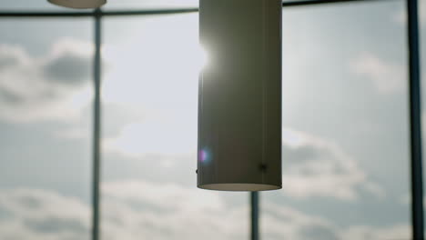 sunlight streaming through large windows creates soft glow on cylindrical pendant light in contemporary gallery with blurred glass and shadows casting gentle ambiance over interior scene
