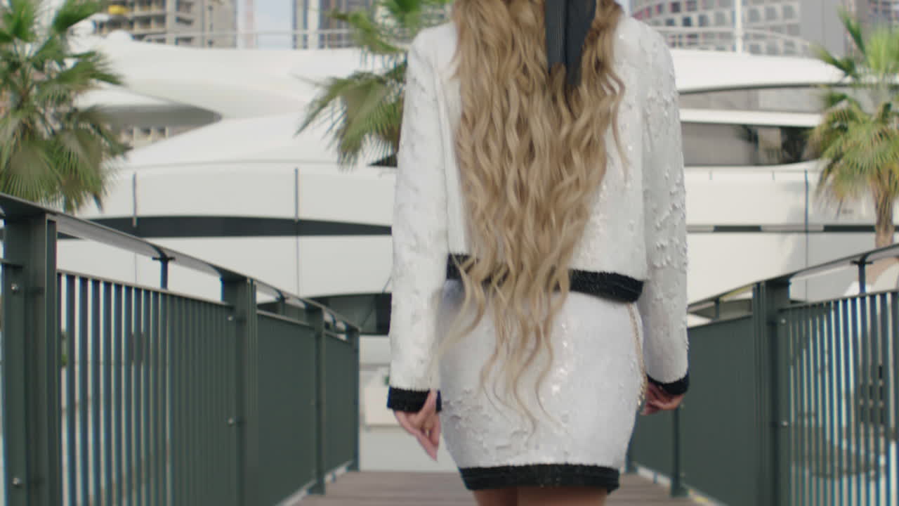 Rear view of luxury woman walking towards yacht in Dubai - Construction site of skyscraper buildings in background - Slow motion