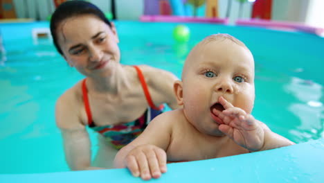 cute lovely caucasian baby holding a toy in the swimming pool. female coach holding a child in water and smiling.