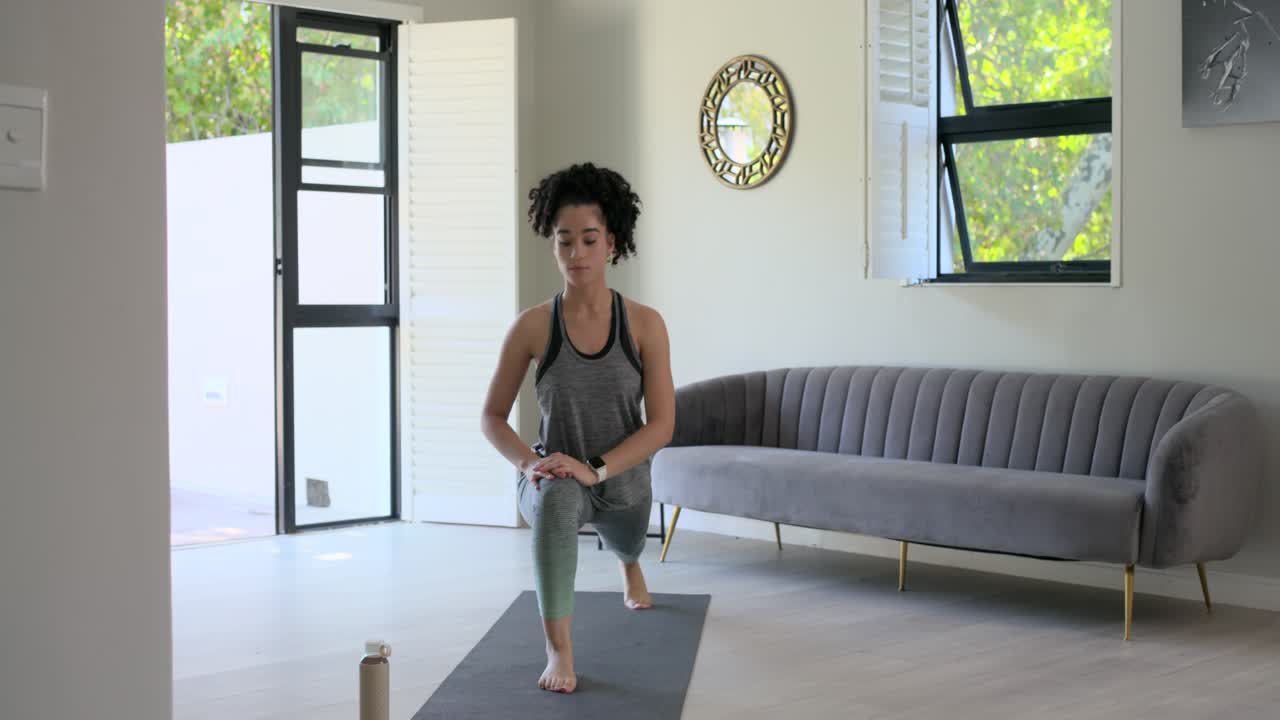 Mulher de roupa esportiva sob o sol da sala de estar, alongando-se para a direita, fazendo afundo no tapete, respirando para o equilíbrio