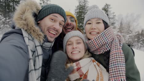 pov portrait of happy friends hikers taking selfie looking at camera in forest in winter