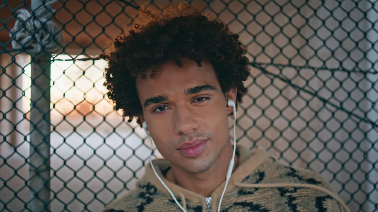 Urban guy listening music in headphones standing street windy evening closeup.