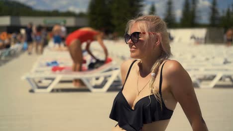 close-up travelling blonde girl is sitting on deck chair on beach in sunglasses