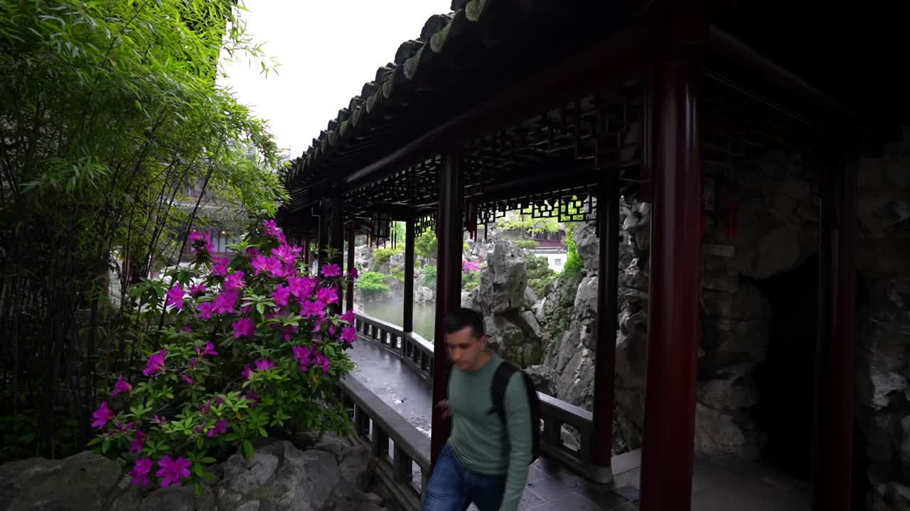 Slow motion of a tourist walking along a walkway over a pond in Yuyuan Garden, taking in the traditional scenery of Shanghai, China