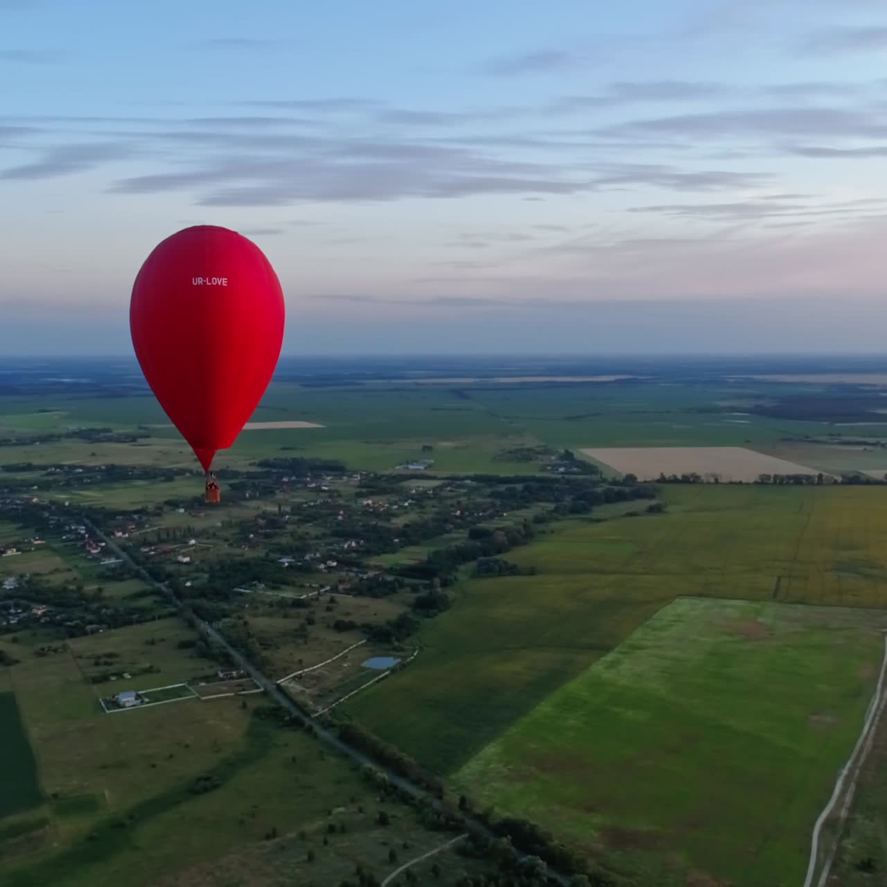 Red aerostat against the setting sun. Hot air balloon flying in the sky over the field in the countryside. Hot air balloon in the form of a heart. Aerial view.