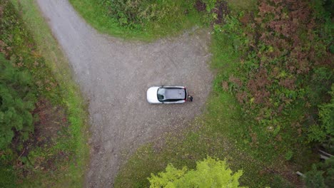 aerial view of a person walking to a suv trunk at a forest parking lot - overhead, drone shot