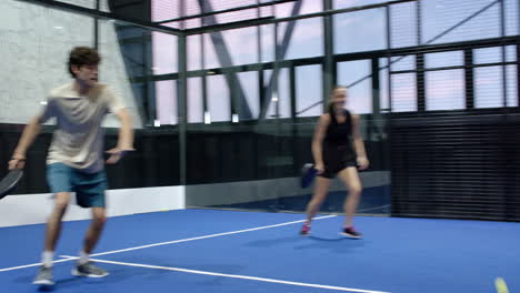 young woman playing padel tennis, smiling and walking on blue indoor court