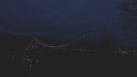 lion's gate bridge connecting vancouver bc to north vancouver from stanley park at night with traffic lights moving across spanning over ocean inlet slow pan left to right creepy peaceful dark relax