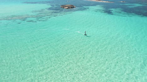 Aerial-View-Of-Male-Tourist-Surfing-Across-Waters-Off-Cala-Escondida-Coastline-On-Electric-Surfboards