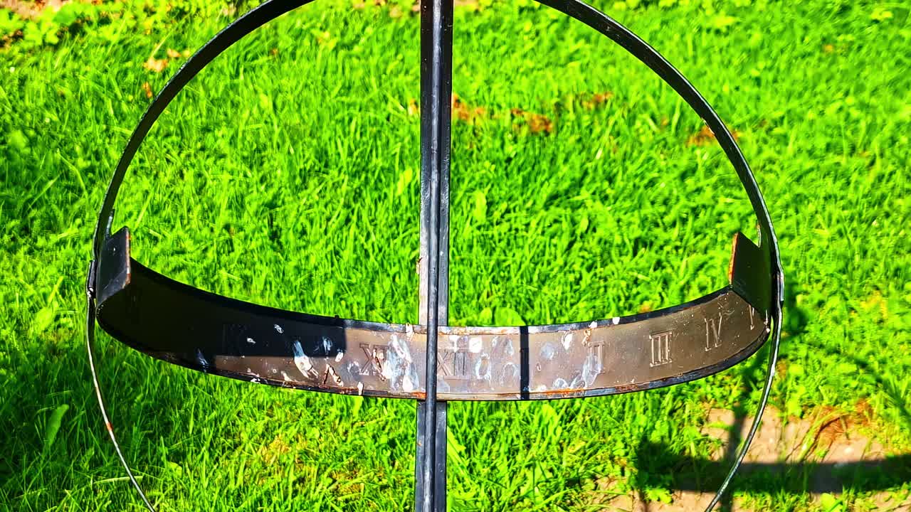 Metal sculpture resembling globe or compass placed on bright green grass outdoors