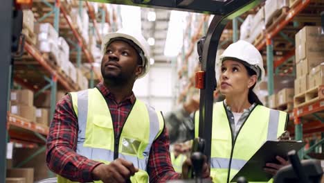 diverse warehouse workers, a man operating a forklift and woman with a clipboard, discuss logistics