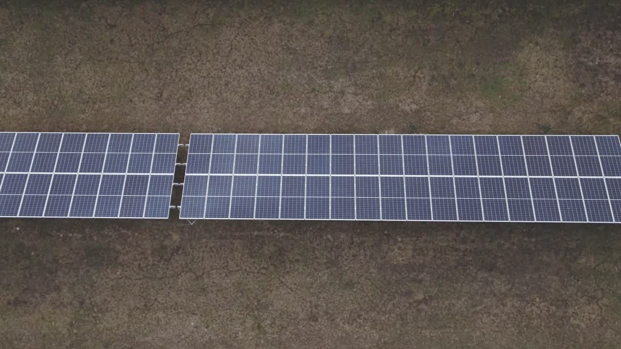 Flying over an extensive solar farm featuring rows of photovoltaic panels installed on open farmland.