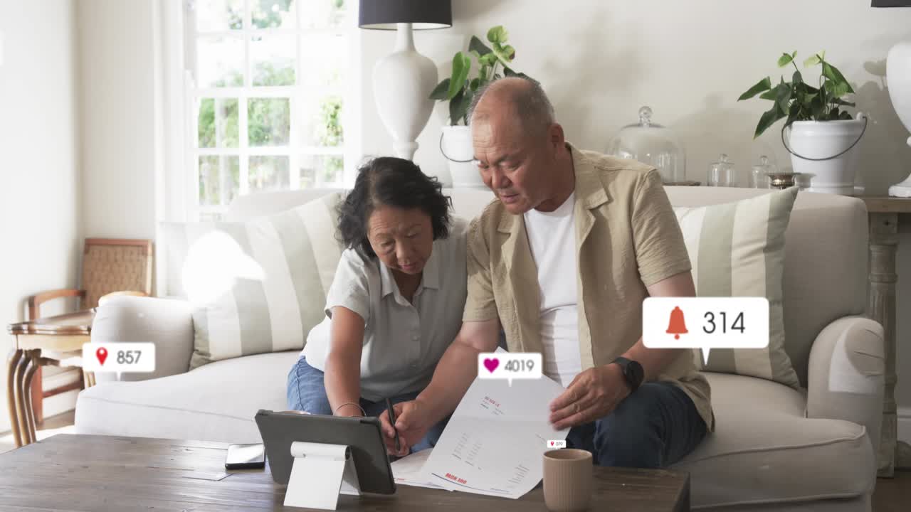 Senior woman and mature man responding as alerts appearing, reviewing finance on tablet, marking