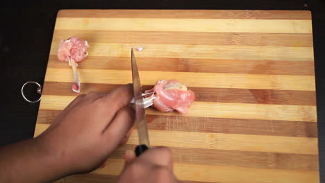 men-cutting-raw-chicken-wings-with-a-sharp-knife-and-shaping-into-a-lollipop-on-a-chopping-board-preparing-for-food