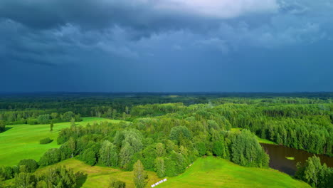 dark grey blue storm clouds gather above bright green forested hillside
