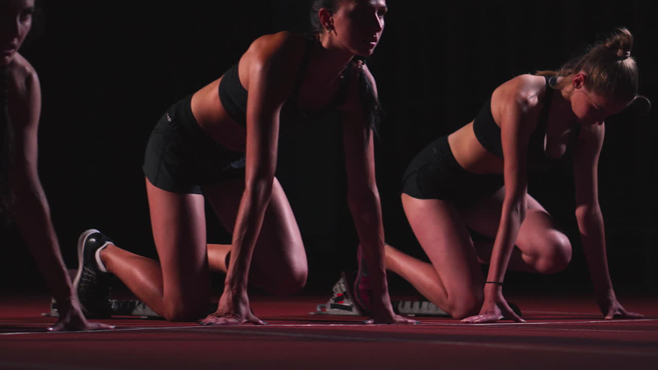 Three sports girl athletes at night on the treadmill start for the race at the sprint distance from the sitting position