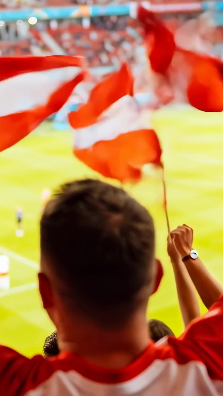 Video verticale: Uomo con maglia rossa che esulta, sventolando bandiere rosse e bianche sugli spalti, con la partita in corso.