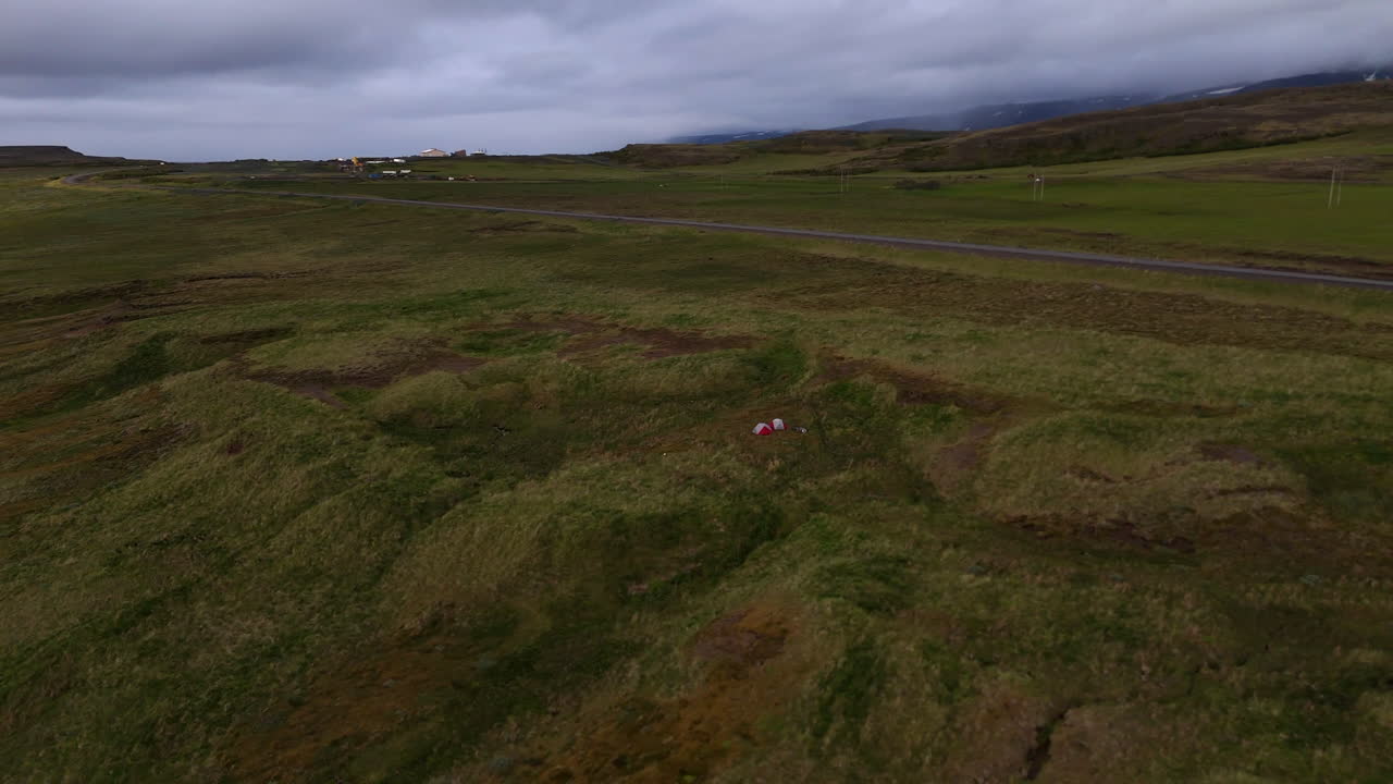 Aerial drone view of Vopnafjörður in Austurland, showing a dramatic coastline, dark cloudy skies, wide open fields, and the calm shoreline of this remote Icelandic region
