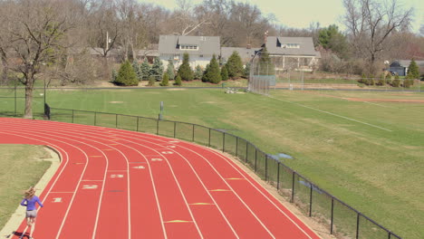 Aerial-camera-descends-towards-track-as-a-teen-girl-runs-past-in-slow-motion