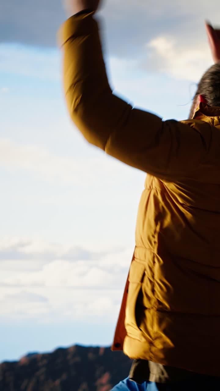 Uomo in giacca gialla che fa stretching sulla cima di una montagna