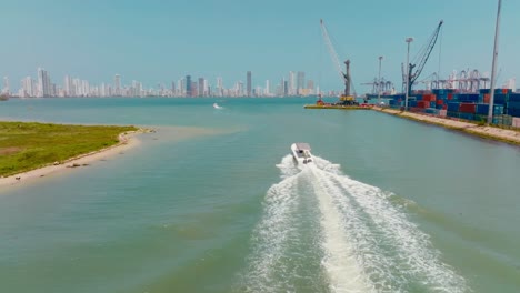 Toma-Aérea-De-Un-Barco-Que-Pasa-Por-El-Puerto-Y-En-La-Parte-De-Atrás-Está-La-Ciudad,-Colombia-Cartagena