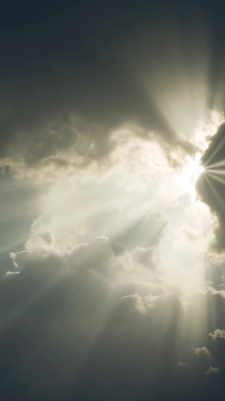 Video verticale: La luce del sole che filtra attraverso una grande massa di nuvole, proiettando raggi nel cielo e creando un effetto a raggiera.