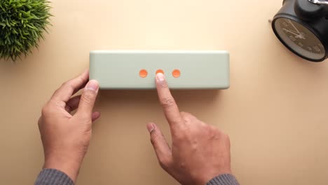 hands holding a light green portable speaker with orange buttons