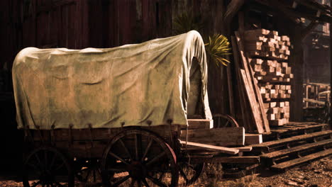 antique conestoga covered wagon near a wooden shed