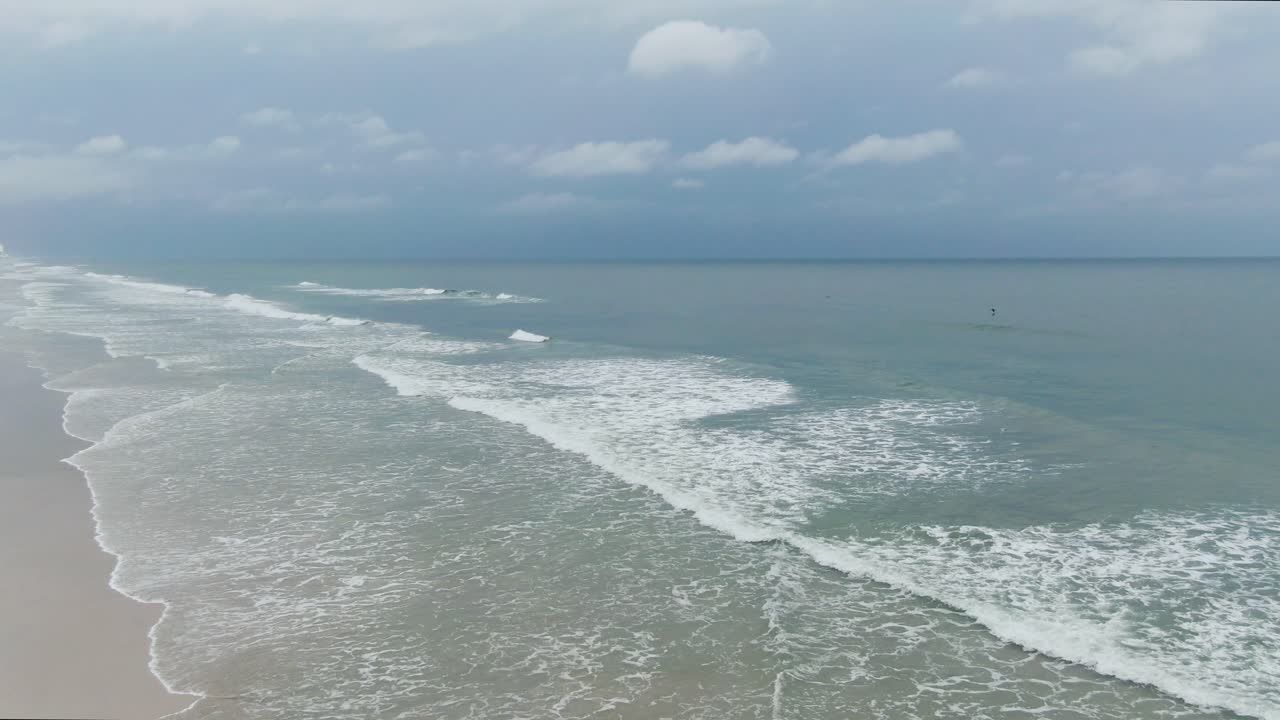 구름이 많은 날에 모래 해변과 개방된 바다를 가로질러 물결이 흐르는 공중 사진