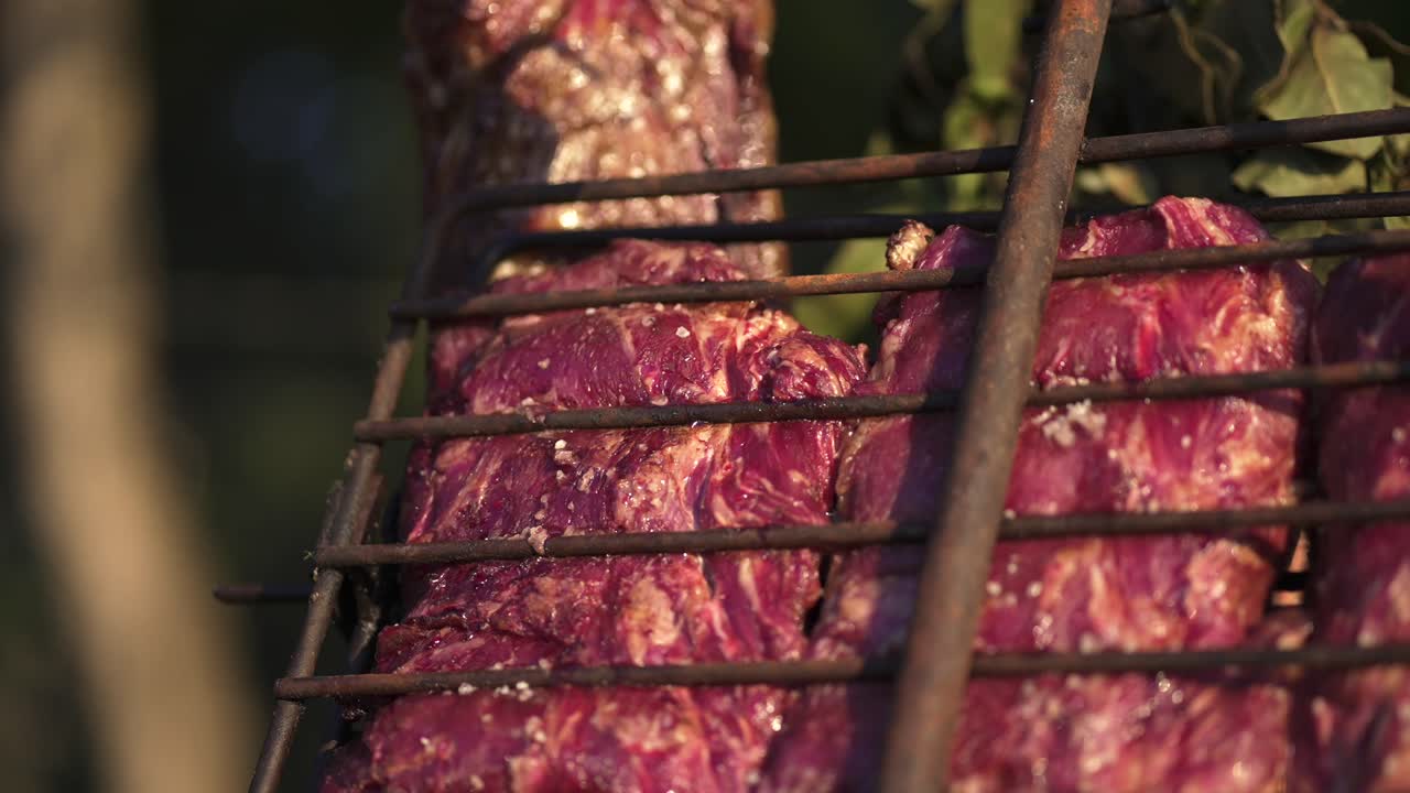 Seasoned beef ribs or skirt steak cuts cooking slowly on a traditional iron cross metal grill, preparing traditional barbecue food with savory flavors for a delicious outdoor meal