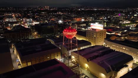 Parallax-aerial-of-Sony-Pictures-studio-lot-water-tower,-entertainment-buildings-at-night