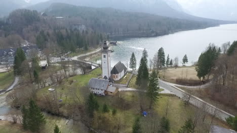 dron elevándose por encima del puente y la iglesia desde el lago bohinj, eslovenia