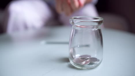 Hand-is-putting-a-coin-into-glass-jar-on-a-blue-background