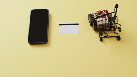 video de un teléfono inteligente con pantalla en blanco, tarjeta de crédito, carrito de compras sobre fondo amarillo