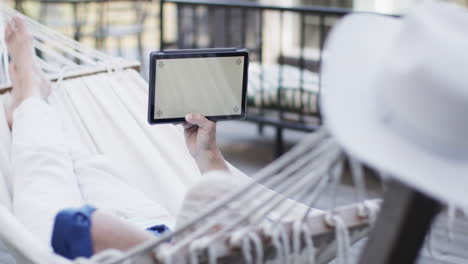 Caucasian-middle-aged-man-using-tablet-relaxing-in-hammock-on-terrace-in-nature,-slow-motion