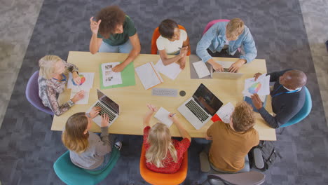 overhead shot of university or college students sitting around table with tutors in lesson