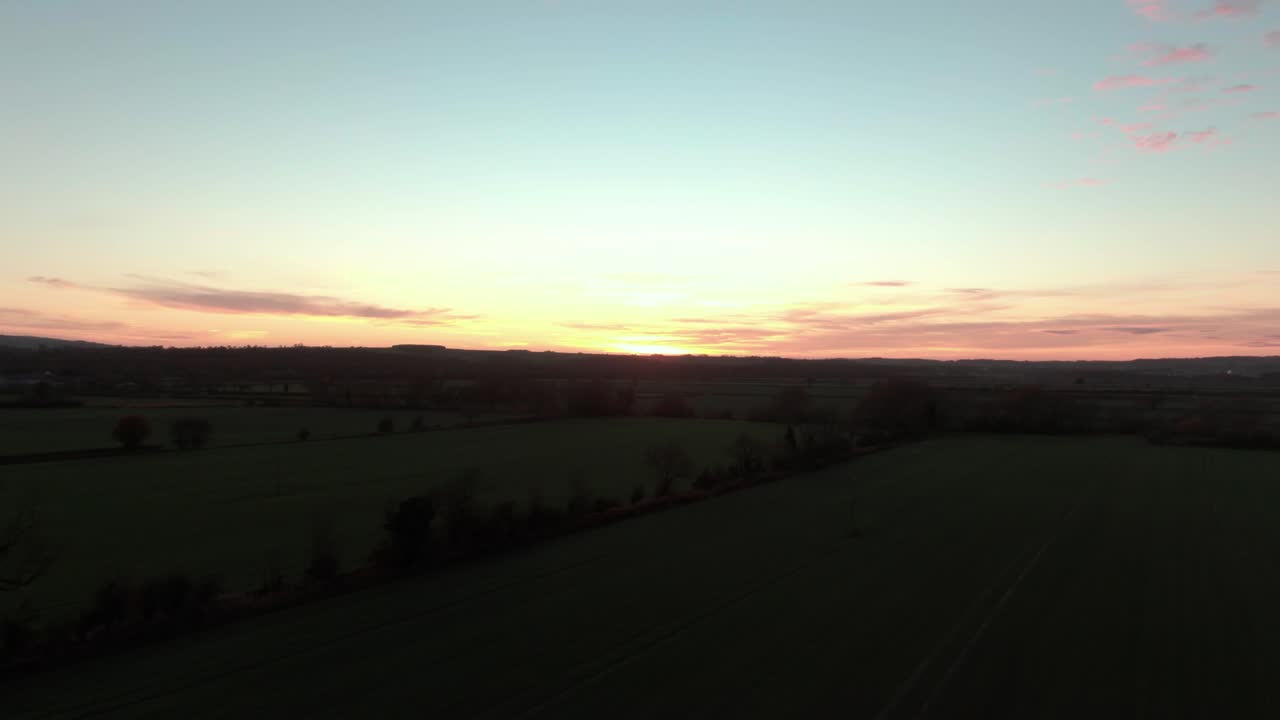 Dramatic and dark drone rise to reveal orange glowing sunset over countryside fields