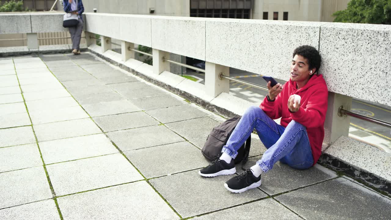 Uomo asiatico che prende uno smartphone, inserisce un auricolare, chiama un amico sulla barriera della piazza, spazio per il testo