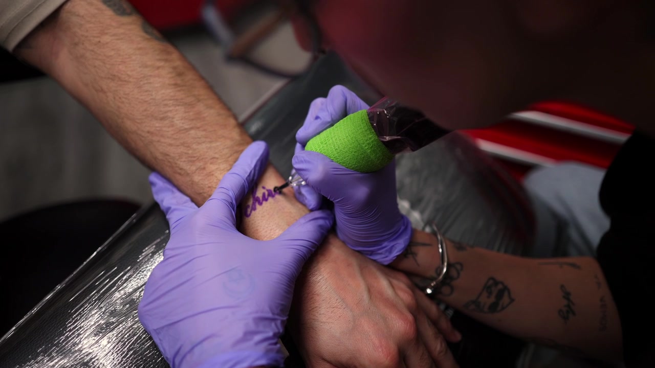 Tatuador aplicando tinta en la muñeca de un cliente en un estudio