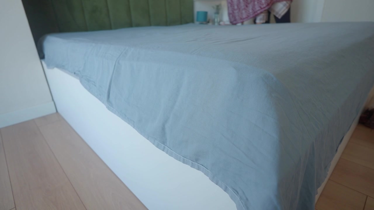 Person Making Bed with Grey Sheet in Modern Bedroom