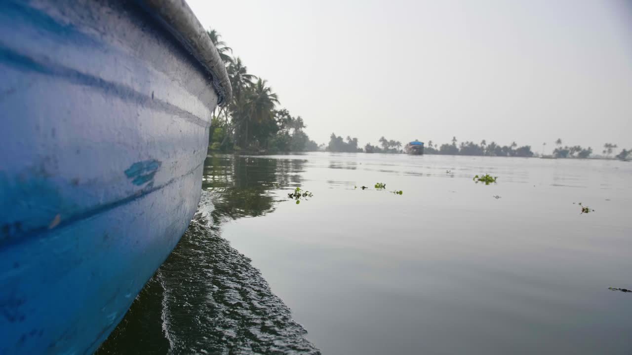 vista desde el lado de un barco en los remansos de kerala a través del agua tranquila en el sol de la tarde con bancos bordeados de árboles y casas flotantes en la distancia